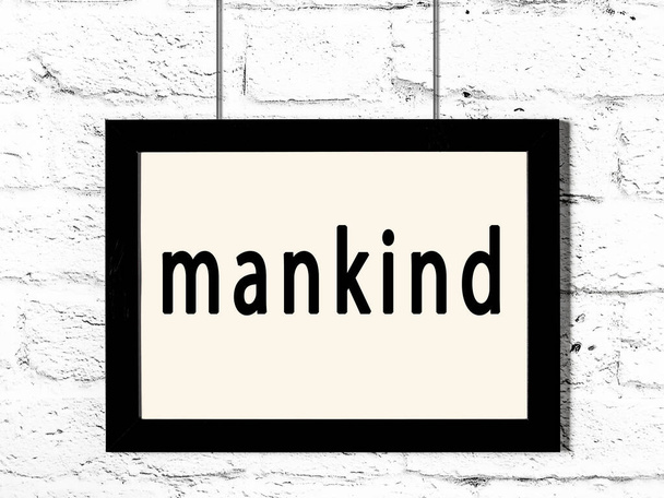 Black frame hanging on white brick wall with inscription mankind - Photo, Image