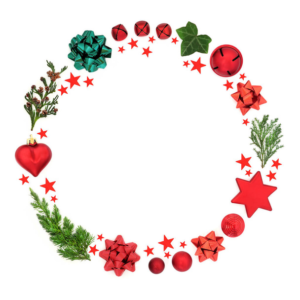 Abstract Christmas wreath decoration with cedar, fir & ivy leaves with baubles, bows & red stars on white background. Festive composition for the holiday season. Flat lay, top view, copy space. - Photo, Image