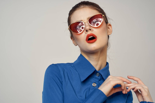 Retrato de una mujer en gafas de sol y una camisa azul sobre un fondo claro recortado vista de Model Copy Space - Foto, Imagen
