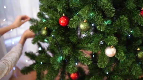 Una mujer joven decora con bolas de Navidad un esponjoso árbol de Navidad en la habitación. Hermoso fondo brillante de Navidad. humor navideño festivo. - Metraje, vídeo