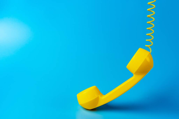 Yellow retro telephone receiver on blue background. - Fotó, kép