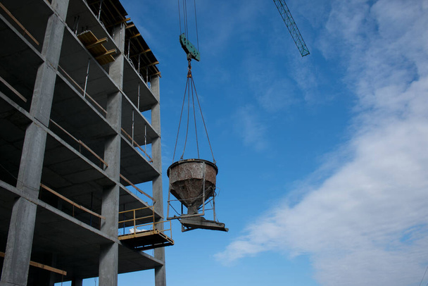 Edificio. Primer plano de una grúa de construcción que levanta un contenedor de hormigón contra un cielo azul. - Foto, imagen