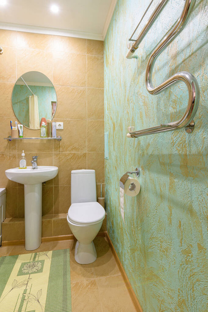 Фрагмент интерьера ванной комнаты, вид на туалет и умывальник, на стене установлен подогреваемый полотенцесушитель - Фото, изображение