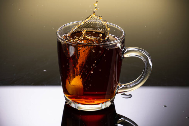 Brew black tea from a sausage bag in a transparent mug with reflection on a gradient background - Foto, Bild