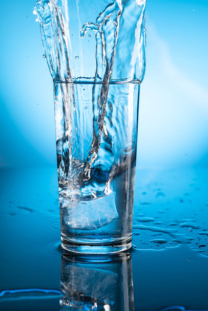 Clear ice water in transparent glass with reflection on blue gradient background - Photo, Image