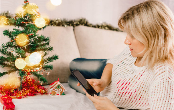 Christmas online shopping. Female buyer makes order on mobile phone. Woman buy presents, prepare to xmas, gift box in hand. Winter holidays sales. - Fotó, kép