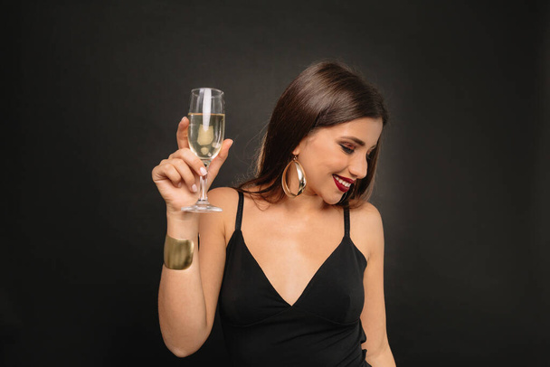 Uma bela jovem no estúdio em um fundo preto com brilhante compõem segurando uma taça de champanhe. Moda, beleza, maquilagem, cosméticos. Foto de alta qualidade - Foto, Imagem