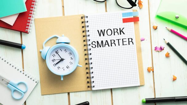 WORK smarter, written in a white notebook on a blue background. Nearby is a diary, multi-colored paper clips and a flower in a pot. Call to action - Foto, imagen