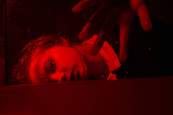 Φρικτό πορτραίτο ενός νεαρού κοριτσιού σε ένα δωμάτιο τρόμου με κόκκινο φως.. - Φωτογραφία, εικόνα