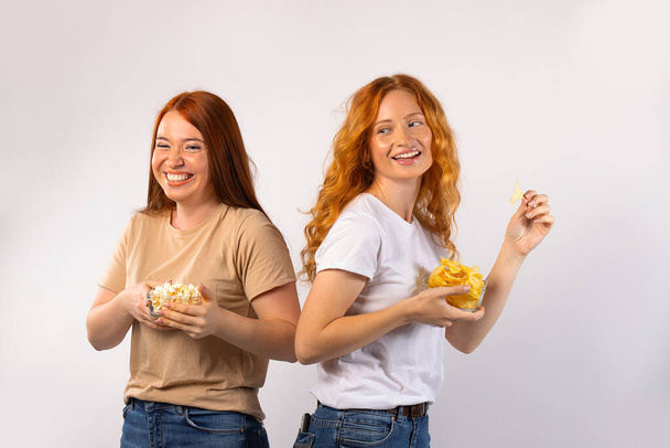 Nice time to spend. Red-haired girls eat chips and popcrn, laugh and loosen up. photo on white background. q High quality photo - Fotografie, Obrázek