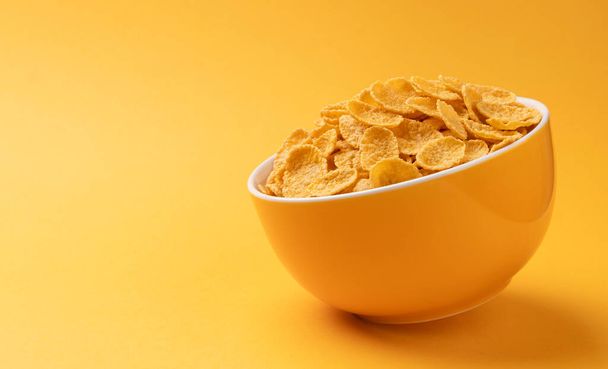 Ceramic bowl of corn flakes on yellow background with copy space - Foto, imagen