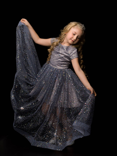 A little girl in a long, elegant dress of a princess on a black background. - Fotoğraf, Görsel