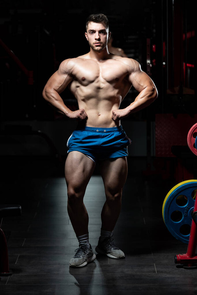 Handsome Man Standing Strong In The Gym And Flexing Muscles - Muscular Athletic Bodybuilder Fitness Model Posing After Exercises - 写真・画像