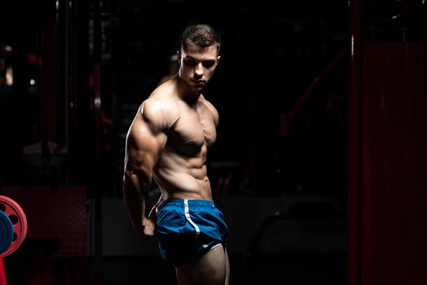 Handsome Man Standing Strong In The Gym And Flexing Muscles - Muscular Athletic Bodybuilder Fitness Model Posing After Exercises - Zdjęcie, obraz