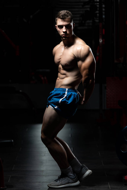 Young Man Standing Strong In The Gym And Flexing Muscles - Muscular Athletic Bodybuilder Fitness Model Posing After Exercises - Foto, afbeelding