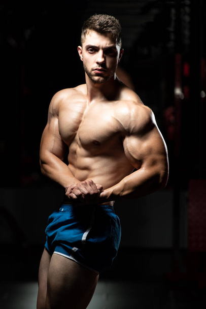 Young Man Standing Strong In The Gym And Flexing Muscles - Muscular Athletic Bodybuilder Fitness Model Posing After Exercises - 写真・画像