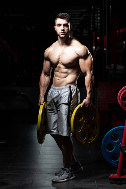 Young Man Standing Strong In The Gym And Holding Weights In Hand - Фото, зображення