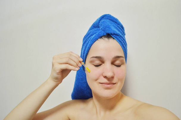 Mujer con una toalla en la cabeza sobre un fondo claro aplica aceite a su cara a través de una pipeta - Foto, Imagen