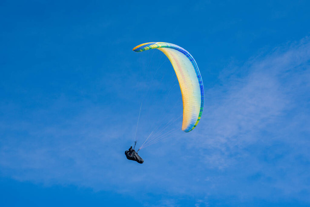 Colourful paraglider flies on a blue sky background. Extreme sport. High quality photo - Photo, Image