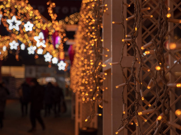 Boże Narodzenie i Nowy Rok świąteczne dekoracje ulic z drzewami i sklepami z wielobarwnych świąt ciąg światła bajki świecące w ciemności na zewnątrz. Koncepcja wiolonczeli ferii zimowych. - Zdjęcie, obraz