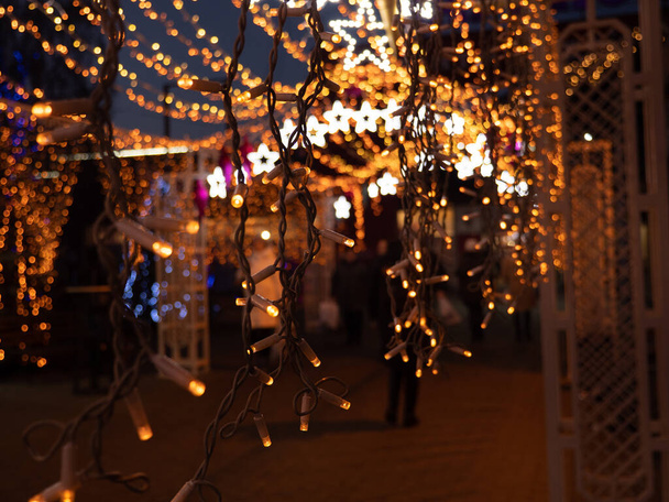 クリスマスと新年の休日は外の暗闇の中で輝く多色のクリスマスストリング妖精のライトを持つ木やお店で通りの装飾。冬休みお祝いのコンセプト. - 写真・画像