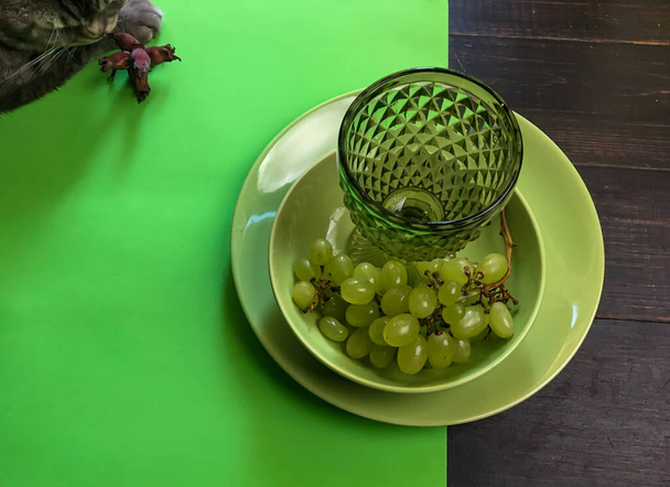 Served wooded table with green wine glass on a green plate with grape - Foto, Bild