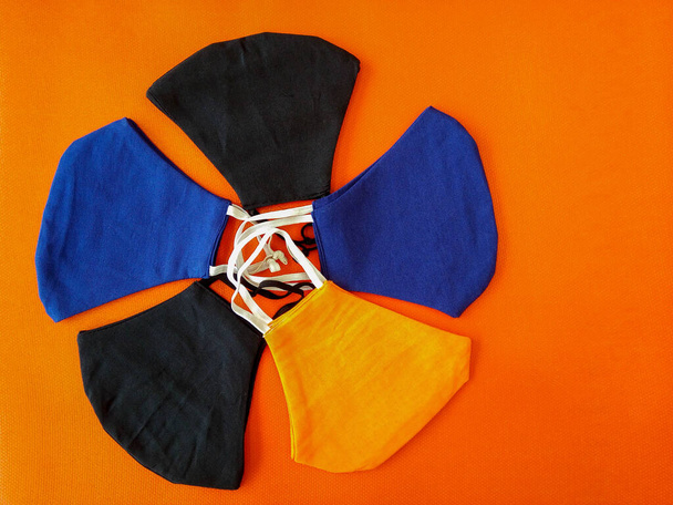 Das Konzept der Handarbeit. Draufsicht, Gesichtsmasken aus Baumwollstoff auf orangefarbenem Hintergrund. Wiederverwendbare Schutzmasken. Husten, Staub, Viren, Bakterien, COVID-19. - Foto, Bild