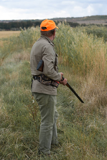 Boerenjager met jachtgeweer loopt door een weiland. - Foto, afbeelding