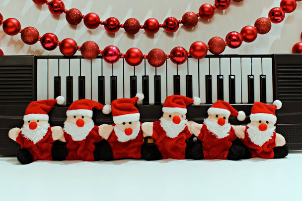 funny santa claus toys on blurred background of piano and christmas garland - Photo, Image