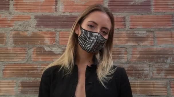 Jovem mulher vestindo máscara facial preto brilhante contra parede de tijolo - Filmagem, Vídeo