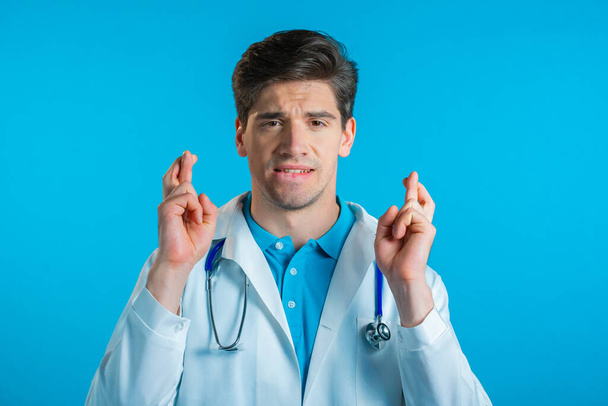 Handsome doctor praying over blue background. Man begging someone satisfy his desires, help with. - Фото, изображение