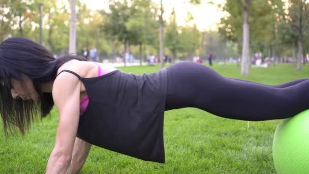 Νεαρή σπορ γυναίκα εκπαίδευση χρησιμοποιώντας μπάλα γυμναστικής στο πάρκο - Πλάνα, βίντεο
