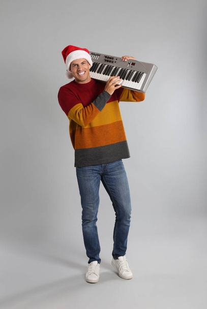 Man in Santa hat playing synthesizer on light grey background. Christmas music - Φωτογραφία, εικόνα