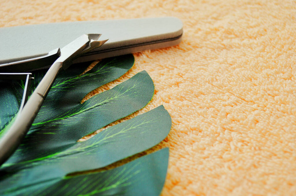 Ногти и ножницы лежат на пальмовом листе на фоне бежевой ткани. - Фото, изображение