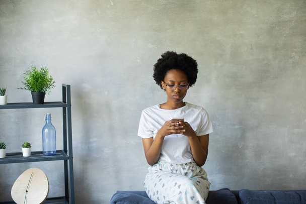 Щаслива афро-американська молода жінка сидить розслаблена на затишному дивані з радістю переїжджаючи в нову квартиру. Посмішка чорна дівчина відпочиває на зручному дивані у вітальні. - Фото, зображення