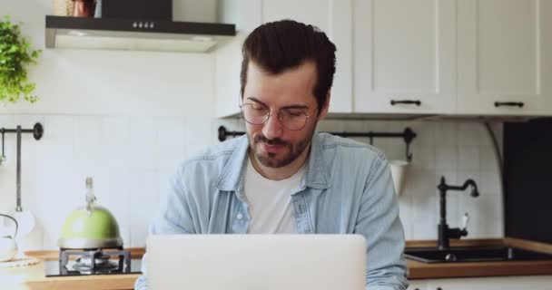 Ευτυχισμένος νεαρός όμορφος άντρας που χρησιμοποιεί υπολογιστή στην κουζίνα. - Πλάνα, βίντεο