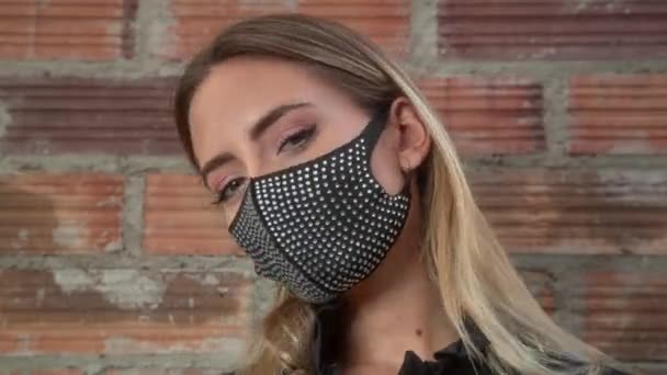 Jovem mulher vestindo máscara facial preto brilhante contra parede de tijolo - Filmagem, Vídeo