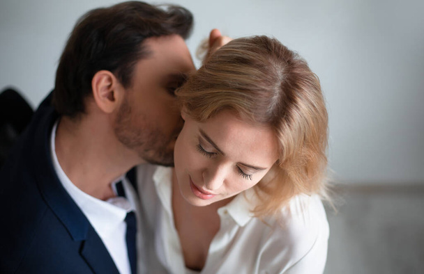 Business man kissing neck of young blonde woman closed eyes. Passion kiss. Enjoyment or workplace romance concept - Foto, immagini