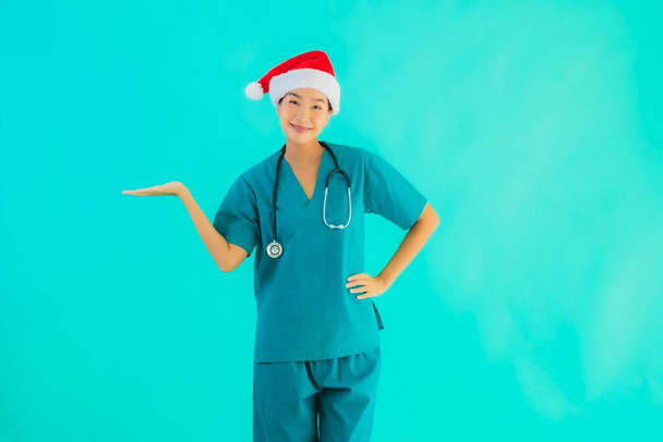 Retrato hermosa joven asiática médico mujer usar navidad sombrero con sonrisa feliz en azul aislado fondo
 - Foto, Imagen
