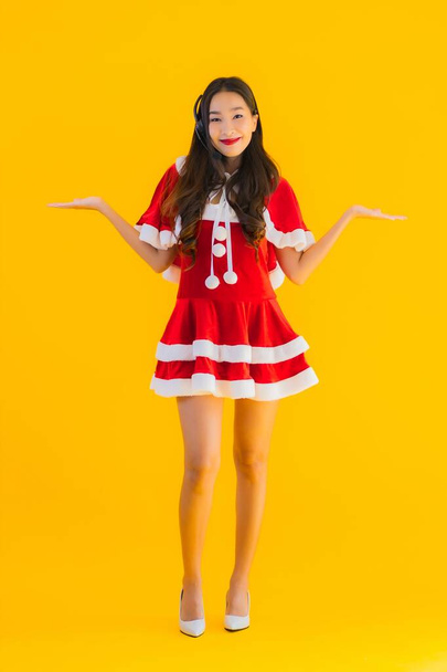 Portrait beautiful young asian woman wear christmas clothes and hat with headphone or headset for call center on yellow isolated background - Fotografie, Obrázek