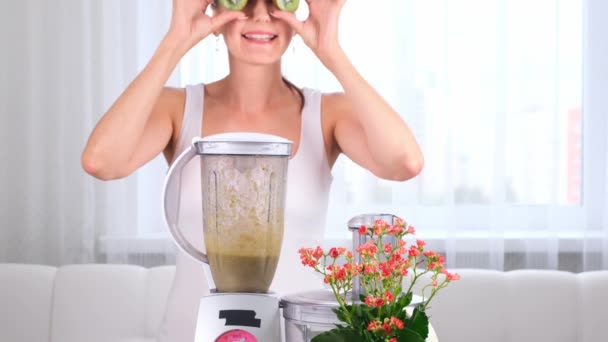 šťastná mladá žena připravuje lahodný výživný koktejl v mixéru. legrační fena dělá oči z kiwi. - Záběry, video