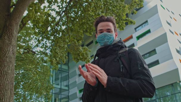 Portrait of a young guy wearing a mask and thank the doctors for their efforts. The teenager stands alone on the street near a modern school or university. Applause in support of health workers during - Photo, Image