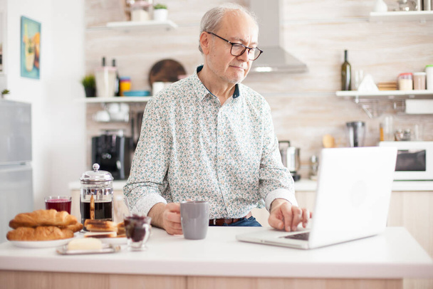 Hombre mayor usando portátil en la cocina - Foto, imagen