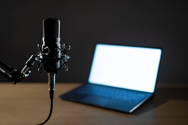 Professional microphone and laptop with white screen in the dark. Equipment in a recording and broadcasting studio - Photo, image