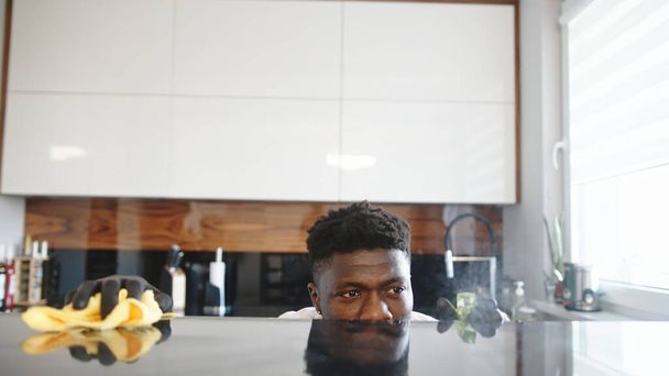 Uomo nero che pulisce cucina. La superficie riflette il suo volto  - Foto, immagini