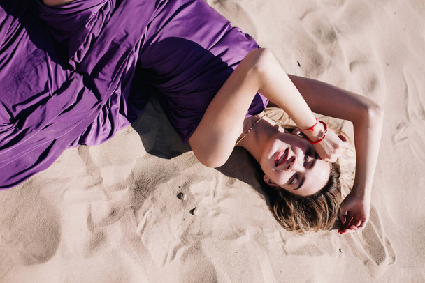 Young, slender girl with purple cloth poses in the desert - Foto, afbeelding