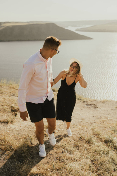 άντρας και γυναίκα ερωτευμένοι περπατούν σε ένα βουνό πάνω από μια μεγάλη λίμνη της θάλασσας - Φωτογραφία, εικόνα