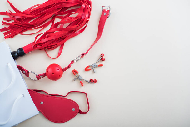 Top view of a red bdsm set in a white paper bag on a white background. Flat lay from sex toys - Φωτογραφία, εικόνα