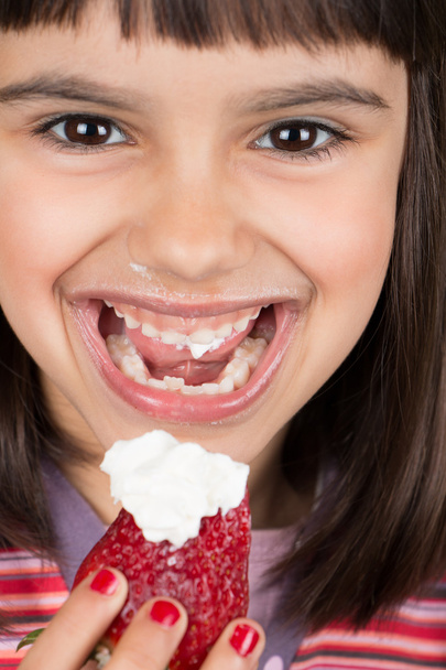 Happy little girl eating a big strawberry with cream - Фото, зображення