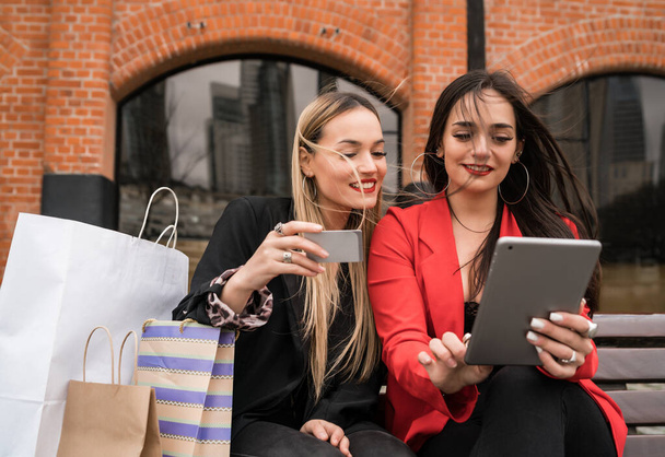 Portrait of two young friends shopping online with credit card and digital tablet while sitting outdoors. Friendship and lifestyle concept. - Foto, Imagen